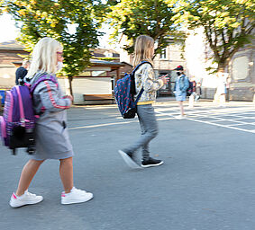 Deux jeunes filles, cartables sur le dos, se dirigent vers leur école.