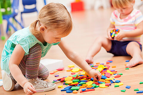 Toddler girls playing with puzzle pieces in a preschool classroom
